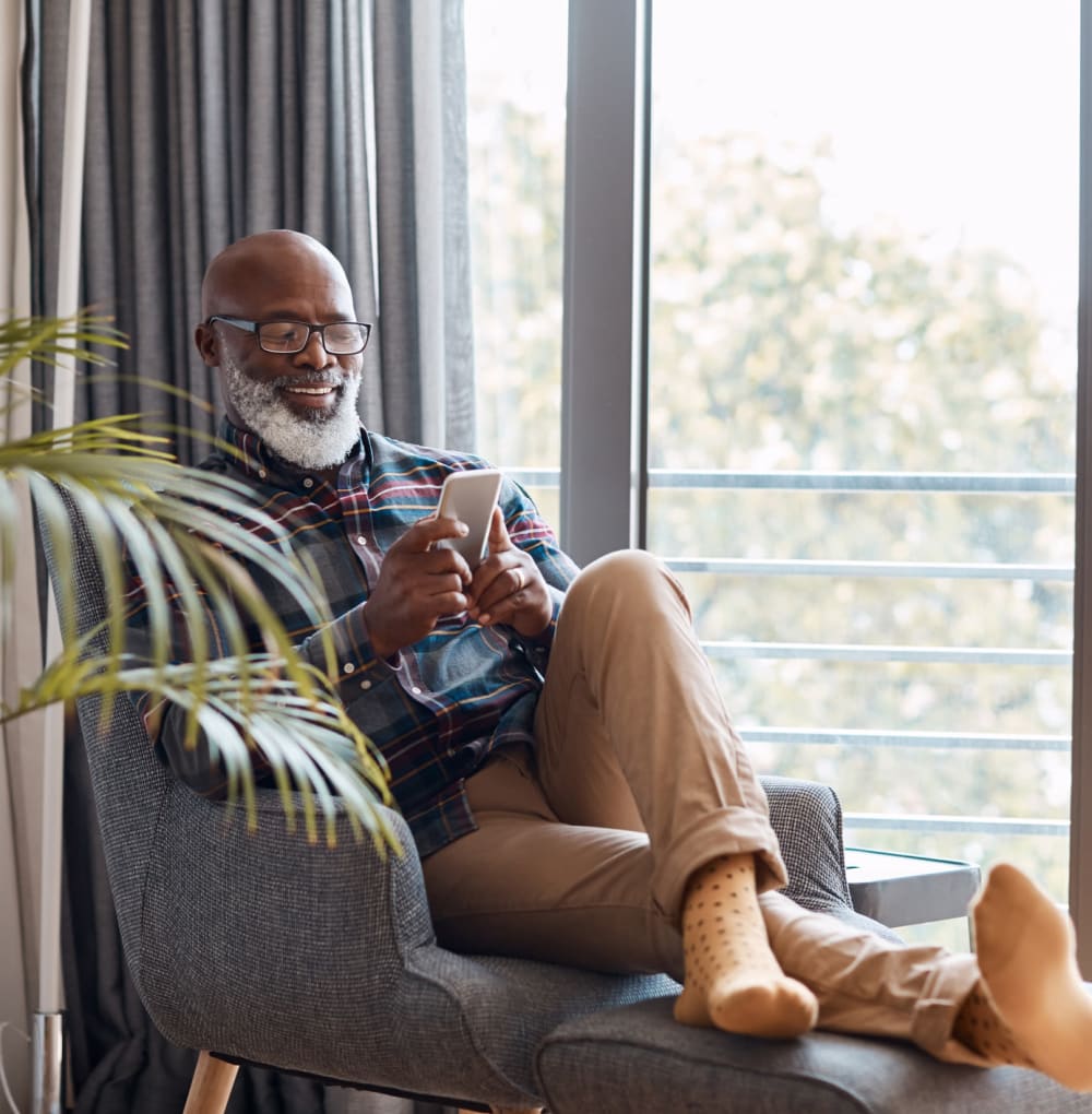 Resident sitting on a recliner chair using a smartphone in his home at a Blossom Collection community