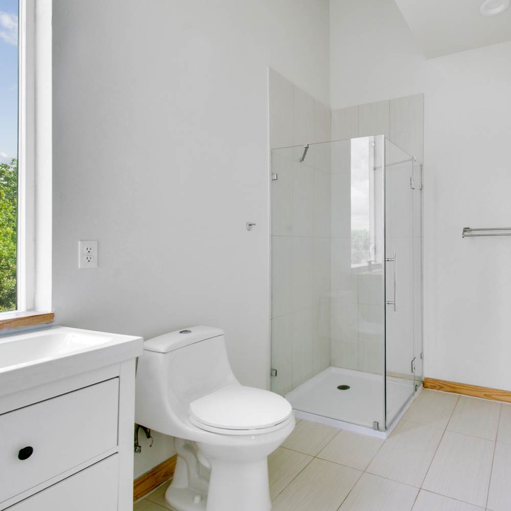 Bathroom with sink, commode, glass shower and large window at The Lofts at 305 in Bryan, Texas