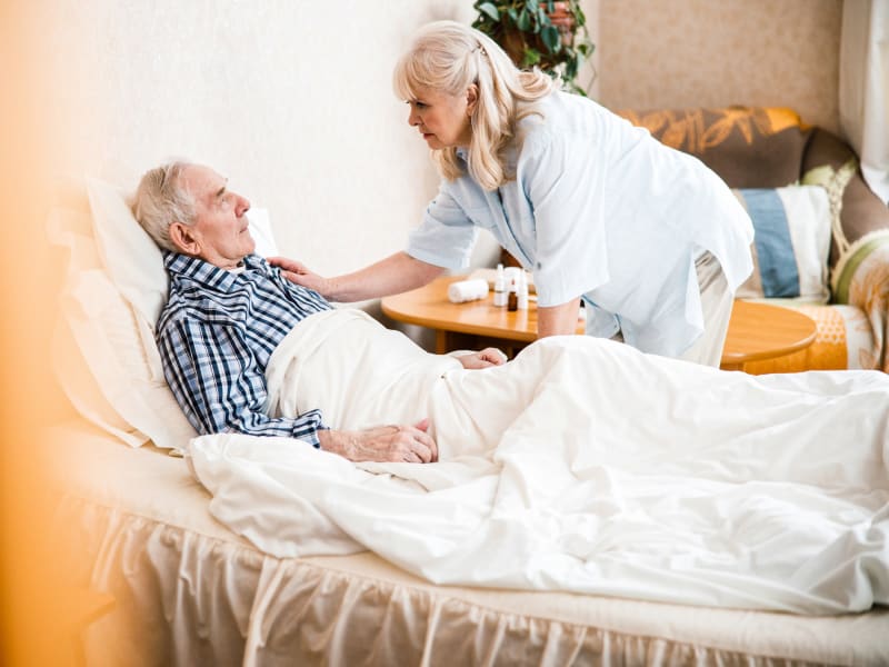 Caretaker comforting a resident who is sitting in bed at a WISH community