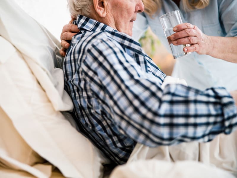 Caretaker assisting a resident with mobility issues in drinking water at Bell Tower Residence Assisted Living in Merrill, Wisconsin