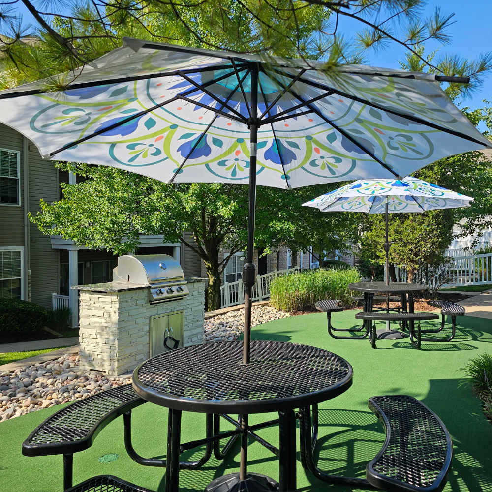 Charming outdoor dining area with vibrant umbrellas and a sleek grill at Boulder Springs in Maryland Heights, Missouri.