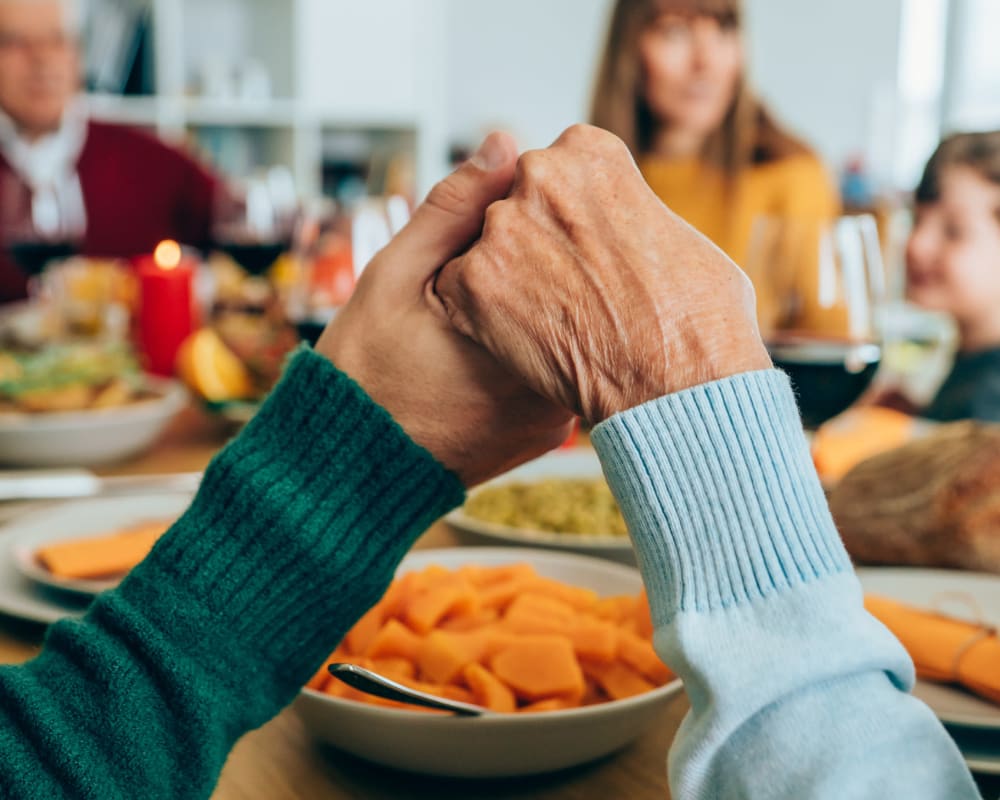 Residents holding hands around a table at Lakeview Terrace of Boulder City in Boulder City, Nevada