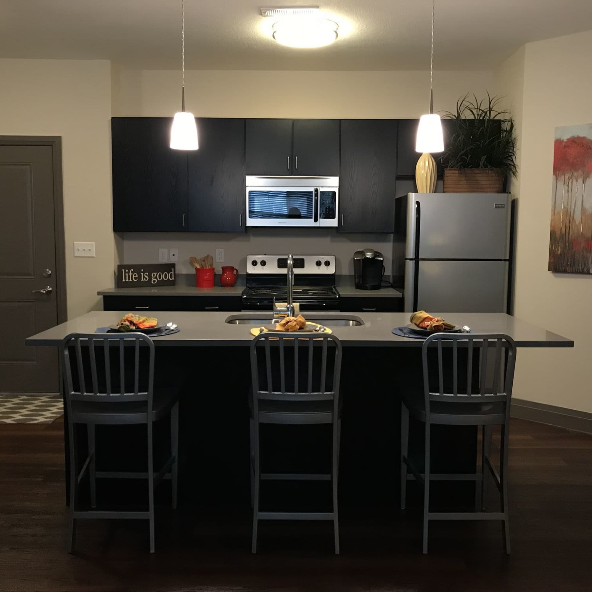 Modern kitchen with granite countertops, stainless steel appliances, and three bar stools at the island at Water Street Apartments in Dayton, Ohio