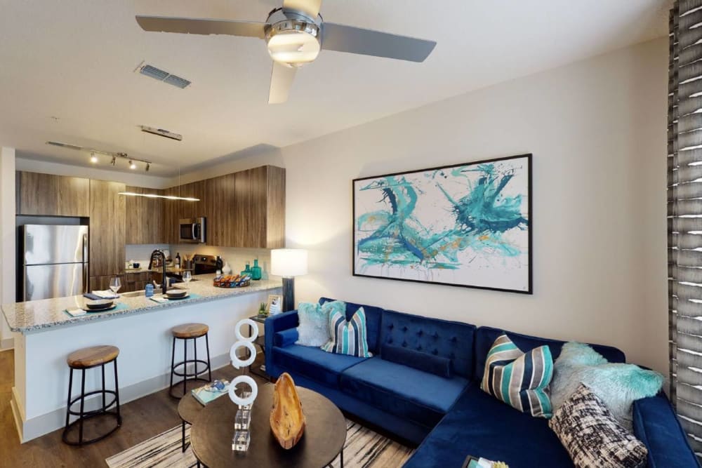 Apartment living room with blue couch, wall art, and ceiling fan at SoBA Apartments in Jacksonville, Florida