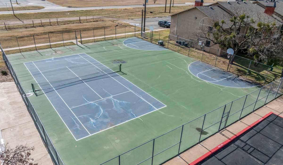 Tennis court with blue and green surfaces, surrounded by a chain-link fence, bright sunny day at Riatta Ranch Apartments in Abilene, Texas
