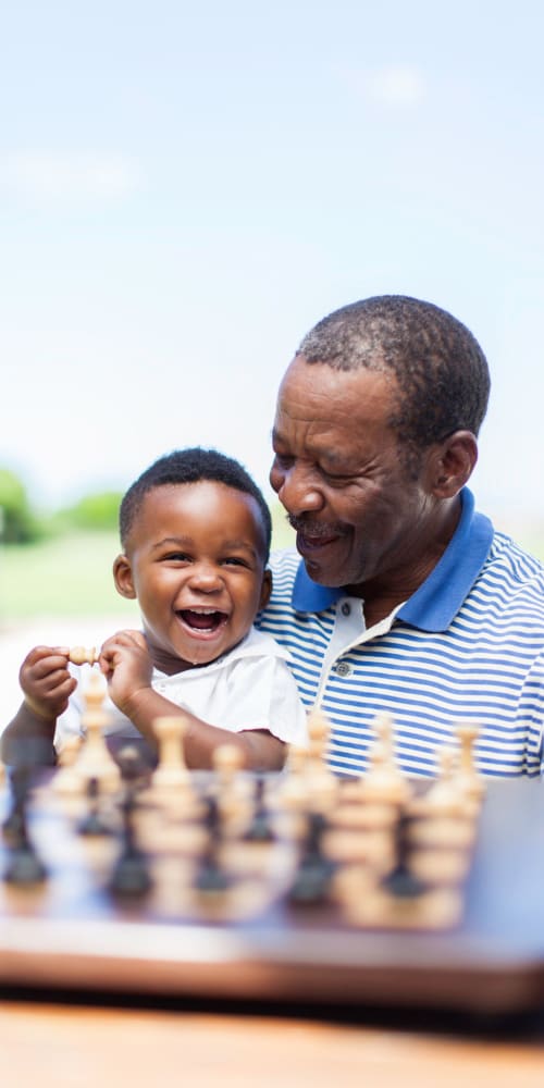 A resident sitting in front of a chess board while holding his smiling young grandson