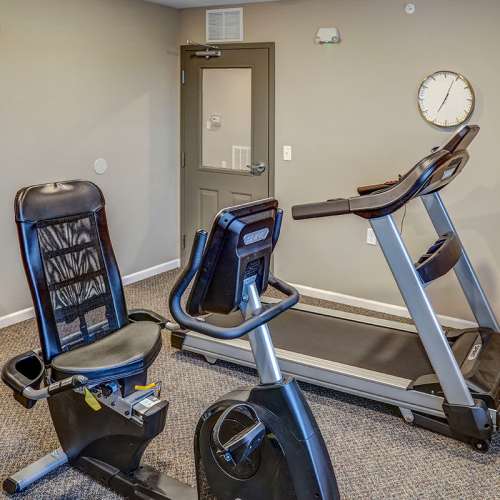 Fitness center with stationary bike and treadmill, carpeted flooring, wall clock, and door to outside at Tristan Ridge in Eminence, Kentucky