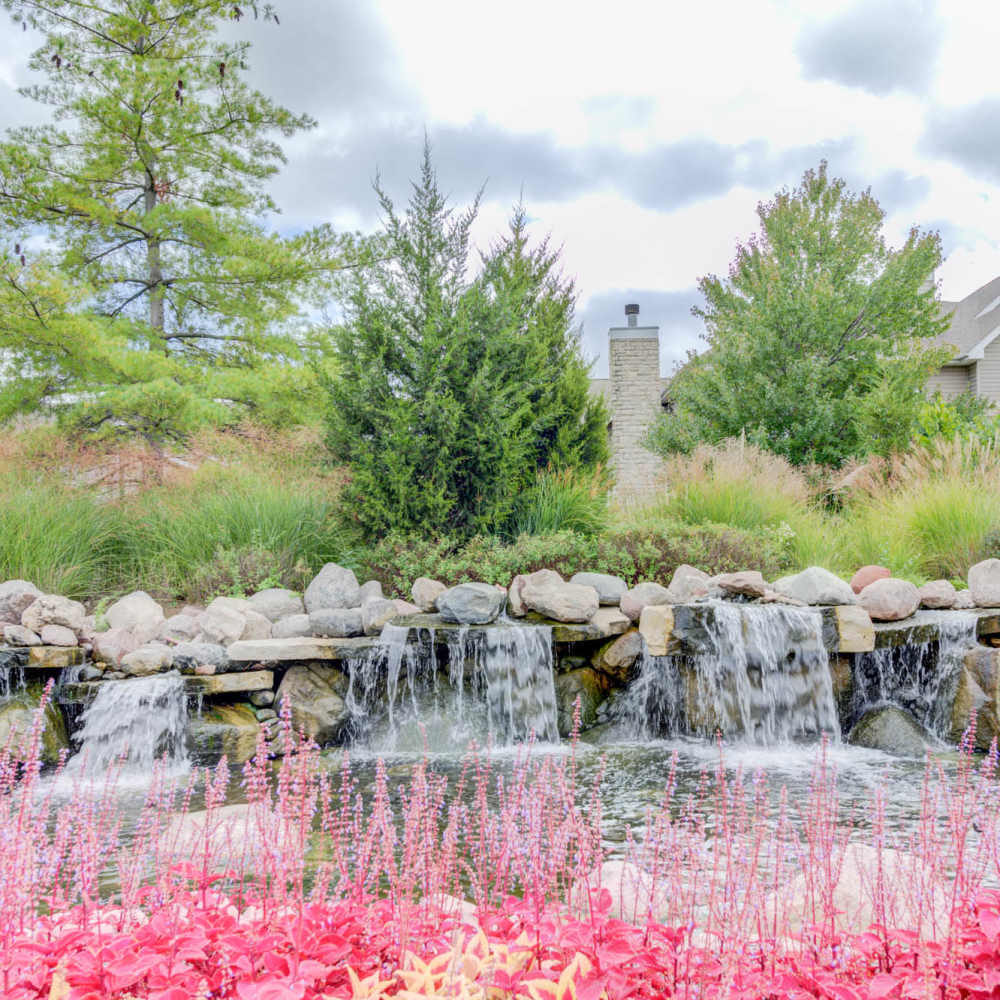 Tranquil water feature surrounded by vibrant flowers and lush landscaping at Boulder Springs in Maryland Heights, Missouri.