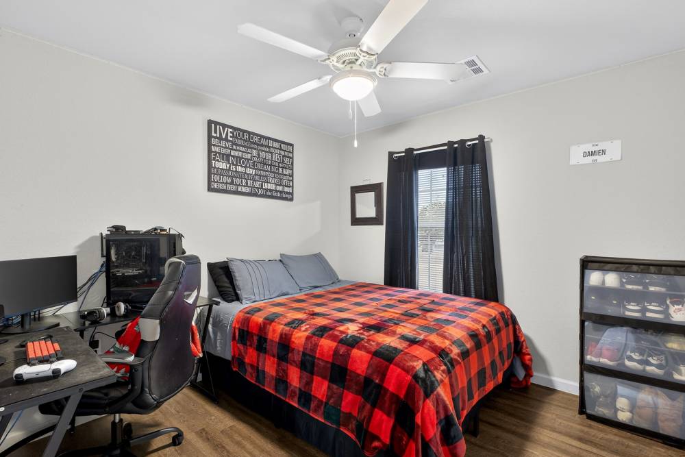 Cozy bedroom with a stylish plaid comforter, modern decor, and ample natural light at Lakewood Crossing in Granbury, Texas.
