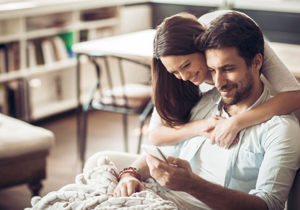 Happy couple surfing the web on a mobile device in their apartment at Sofi Ventura in Ventura, California