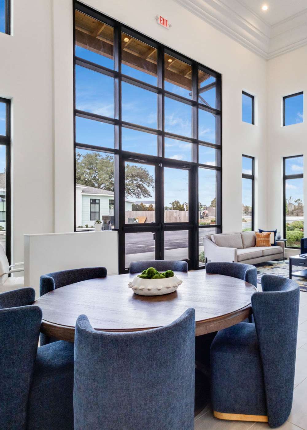 Bright community lounge with large windows, round wooden table, and cozy blue chairs at Lakewood Villas in Bossier City, Louisiana