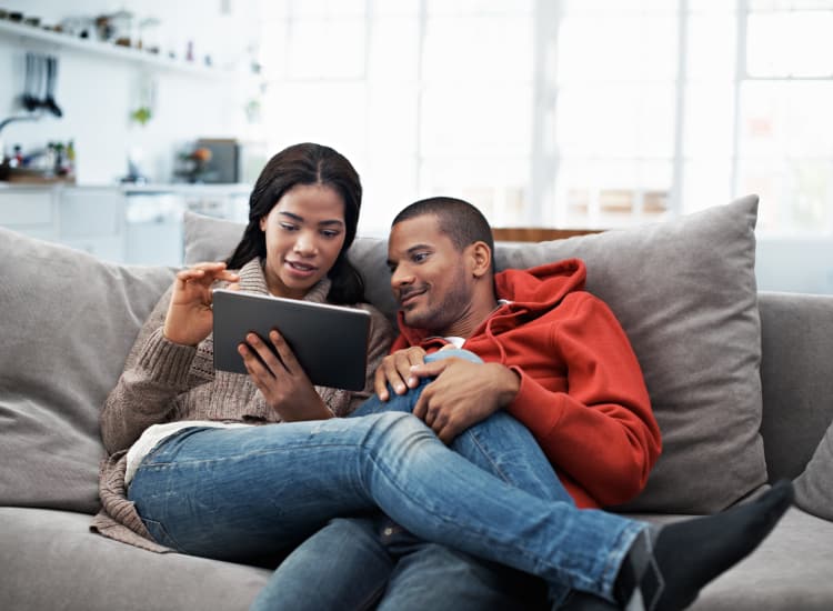 Young couple using their tablet while sitting on the sofa at Warner Village Apartments home in Trenton, New Jersey