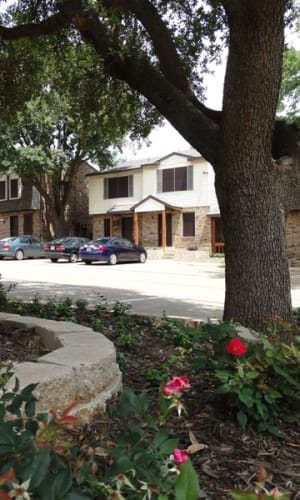 Exterior with ample parking and garden with mature trees at Round Rock Townhomes in Arlington, Texas