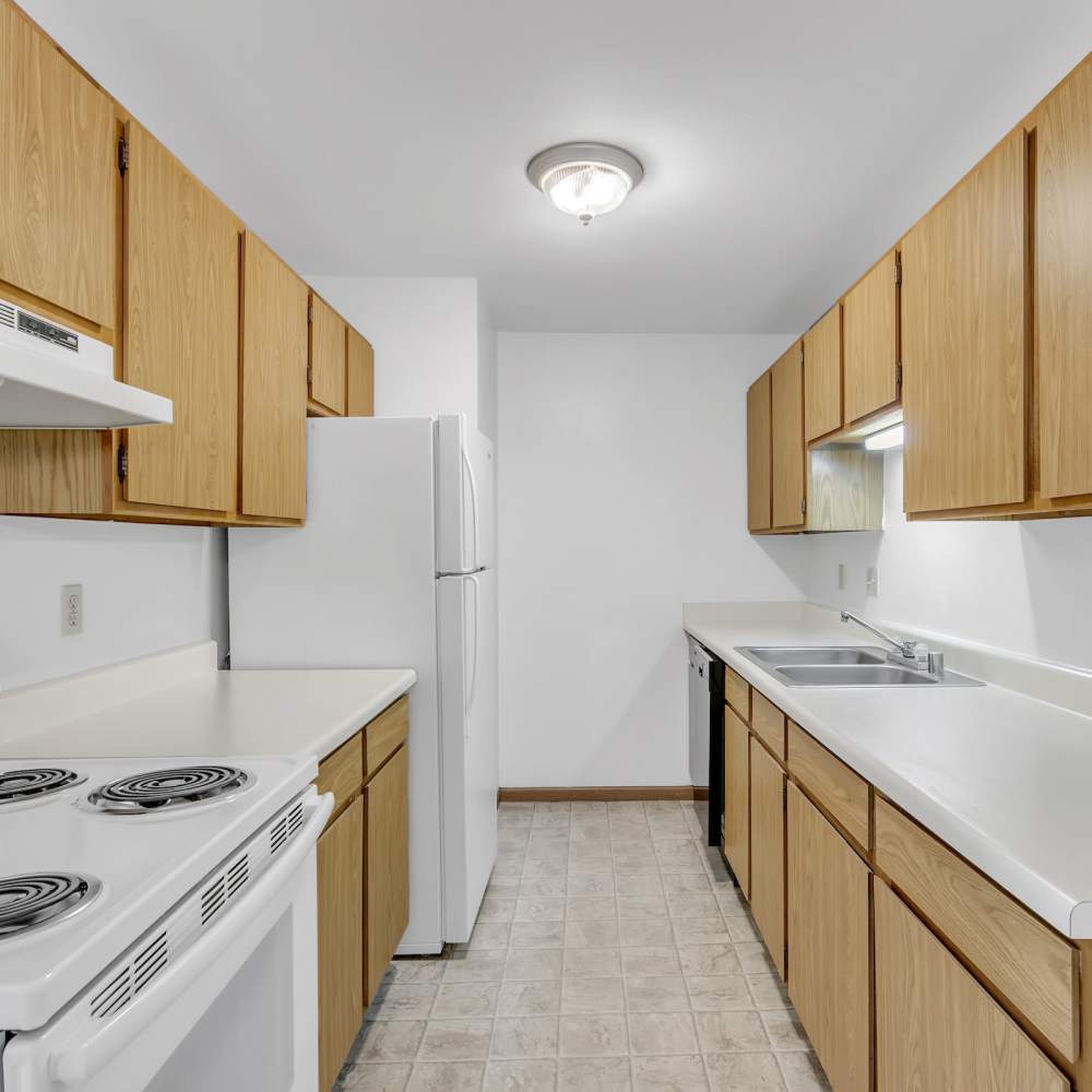 Cozy kitchen with square tiles for flooring, white appliances and brown cabinetry at Prairie Apartments in Salem,Wisconsin