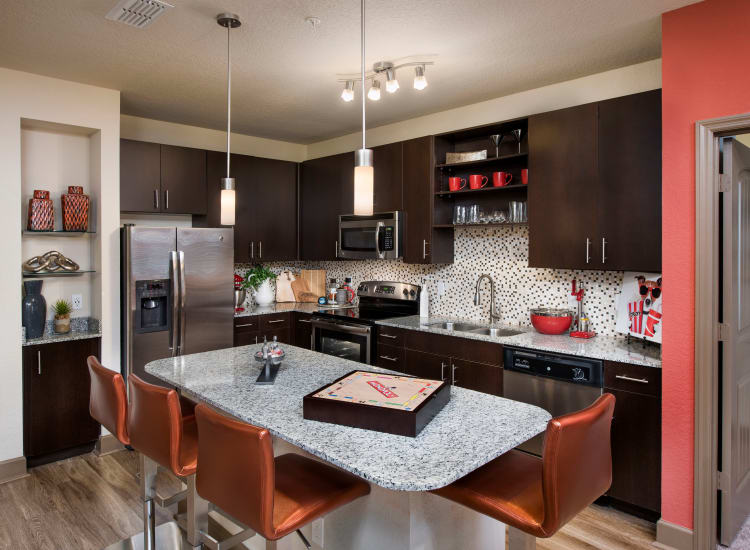 Modern kitchen with granite countertops and dark wood cabinetry in a model home at The Courtney at Universal Boulevard in Orlando, Florida