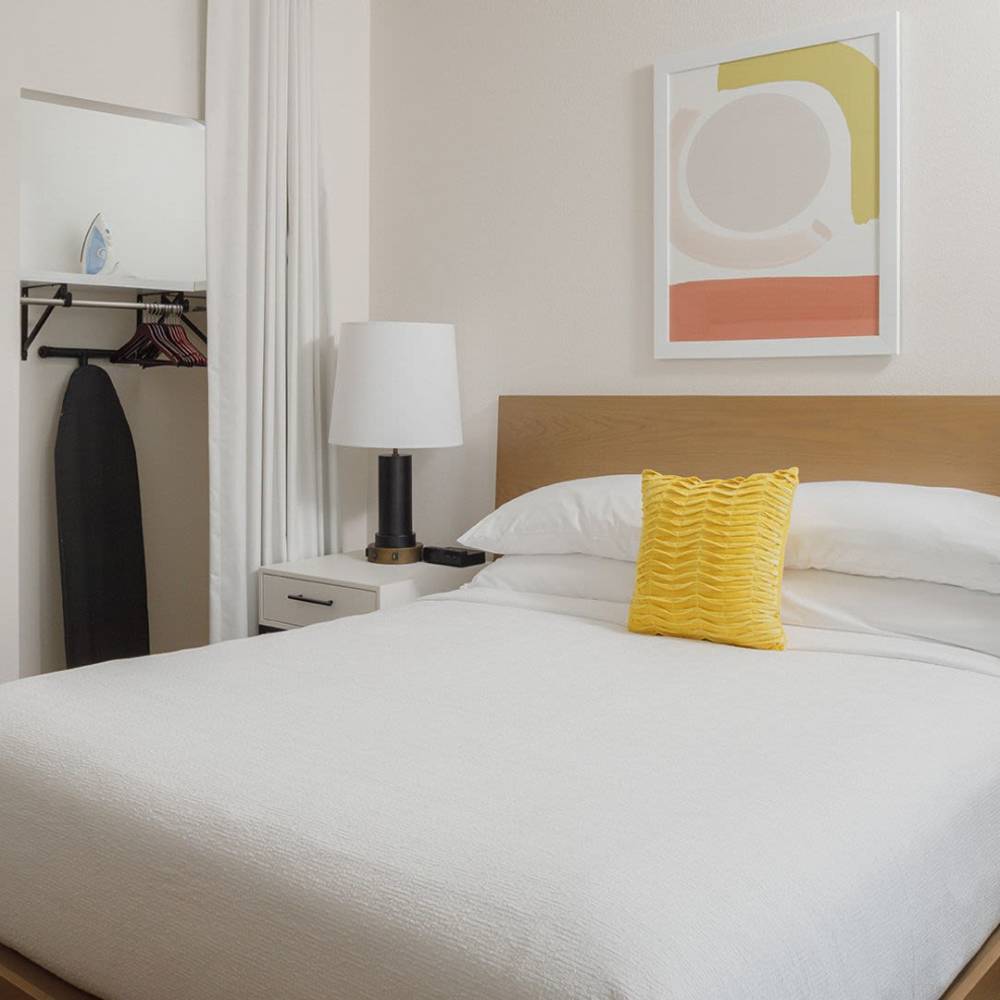 Modern bedroom with white bedding and yellow accent pillow at WaterWalk Jacksonville - Deerwood Park in Jacksonville, Florida