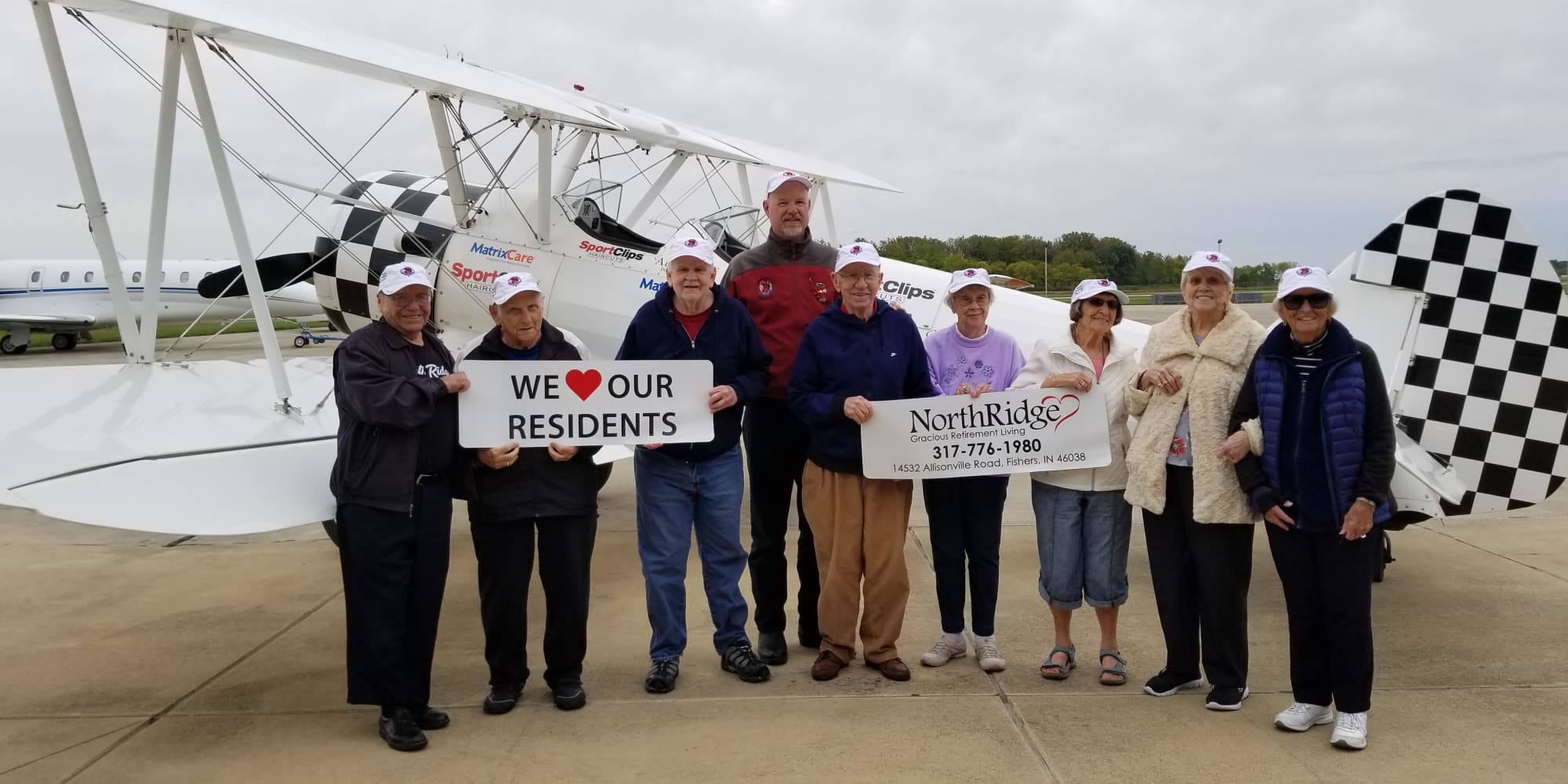 Residents from Northridge Gracious Retirement Living in Fishers, Indiana holding signs in front of a plane
