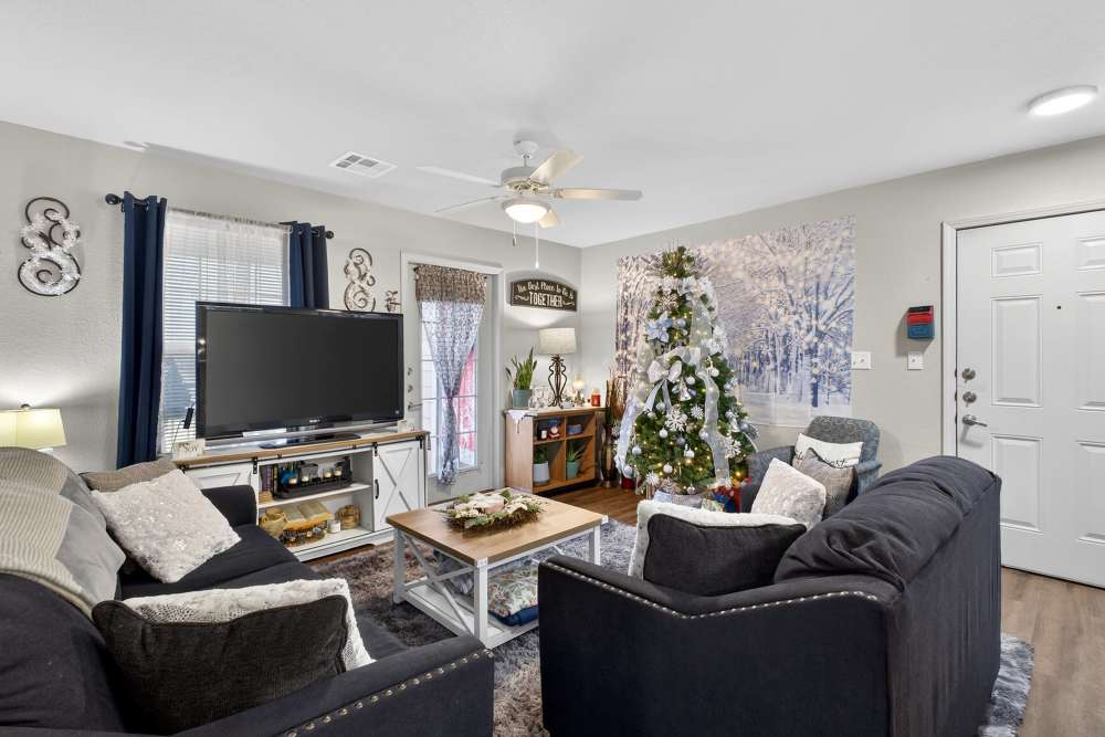 Cozy living area with a festive touch featuring plush seating, a charming holiday tree, and inviting natural light at Lakewood Crossing in Granbury, Texas.