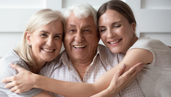 Parents and adult daughter enjoying a group hug at Victoria Park Personal Care Community in Regina, Saskatchewan