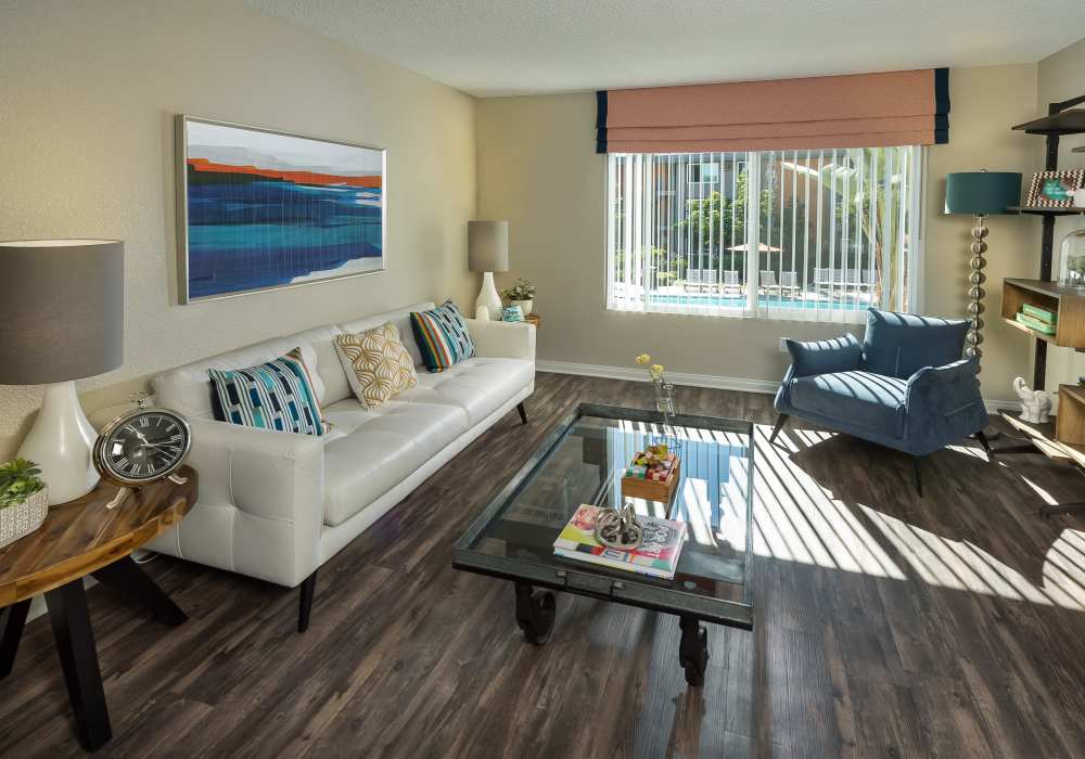 Spacious living room with large couch, coffee table, chair and wood-style flooring at UCA Apartment Homes in Fullerton, California