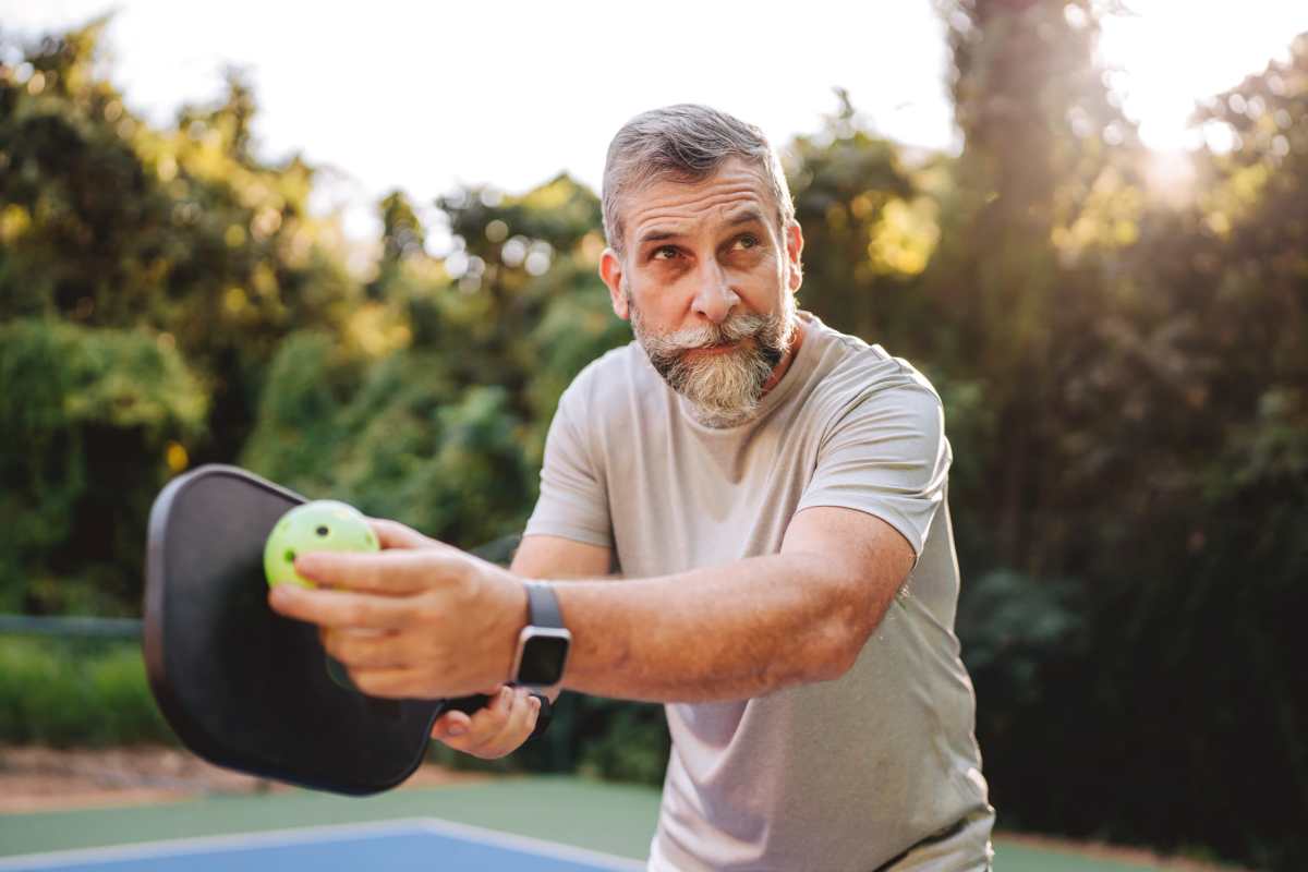 Man playing pickleball outdoors in a lush green setting at Villas At Alexander Bay in Baytown, Texas