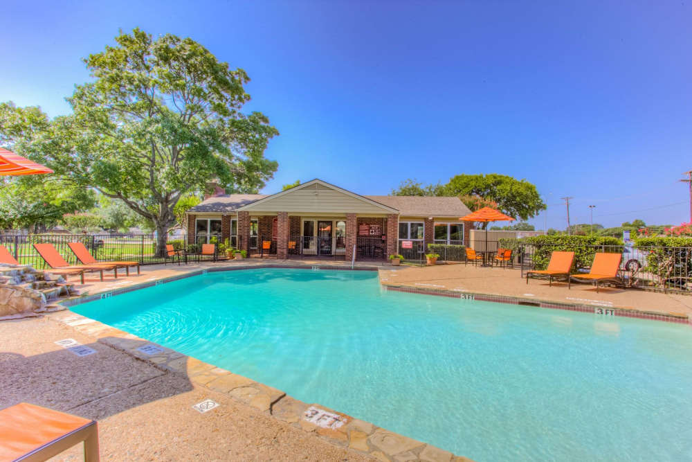 Charming resort-style pool with vibrant orange loungers and lush landscaping at Charter Oak in Euless, Texas.