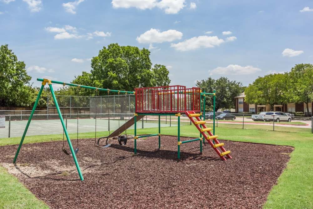 Charming playground with vibrant swings and climbing structure set in lush landscaped grounds at Charter Oak in Euless, Texas.