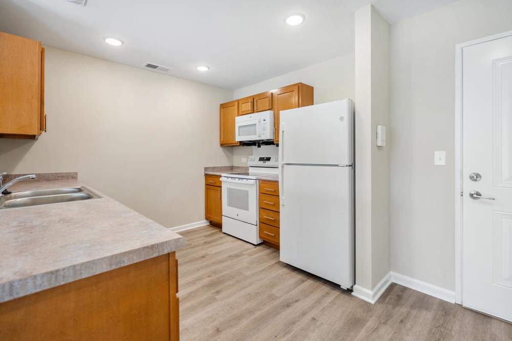 White appliances and wooden cabinets in apartment kitchen at Deville Manor in Oswego, Illinois