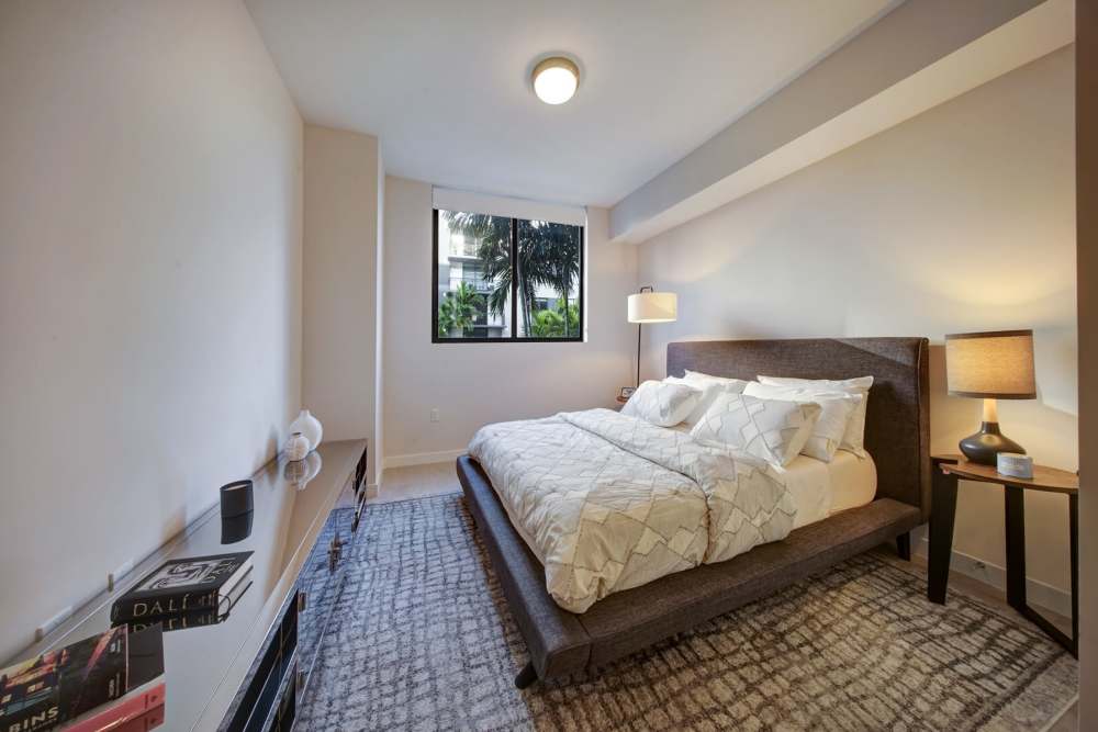 A bedroom with a king-sized bed, nightstands with lamps, and a large window at EON Squared in Fort Lauderdale, Florida