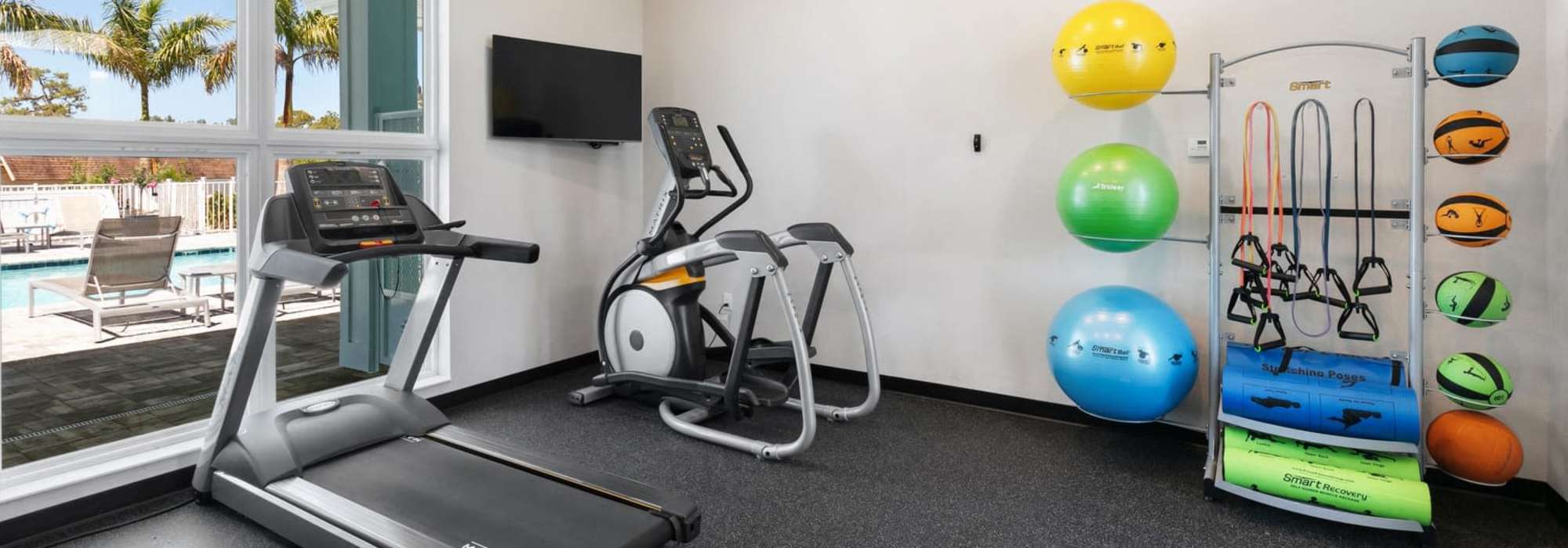 Modern fitness room with state-of-the-art equipment and views of a sparkling water pool at Lemon Bay Apartments in Englewood, Florida.