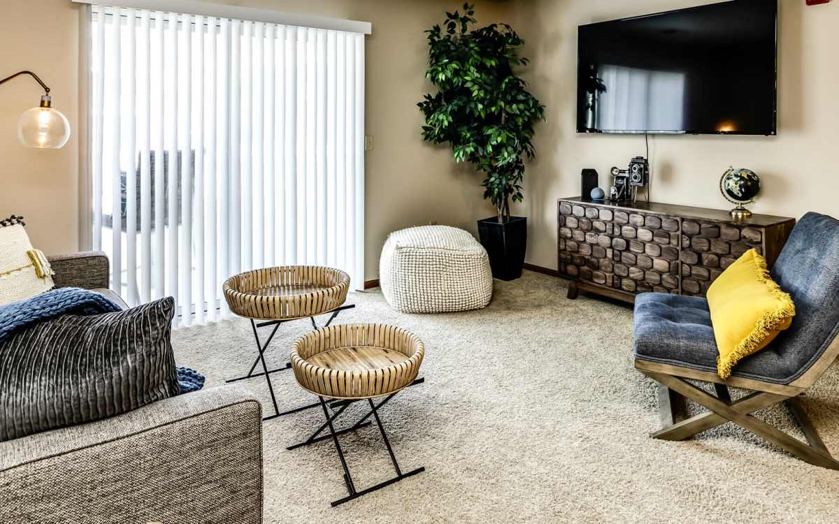 Living room with sofa, plush carpeting, television and door leading to balcony at The Falgrove Apartments in Omaha, Nebraska