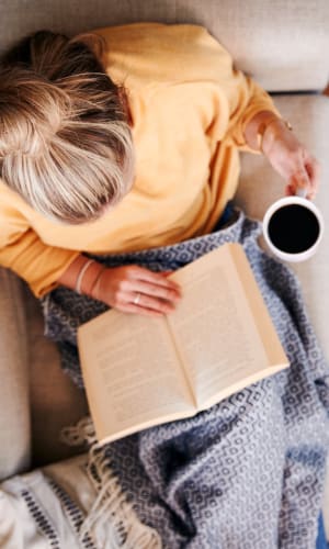 Resident reading and enjoying a cup of coffee on her comfortable couch at Round Rock Townhomes in Arlington, Texas