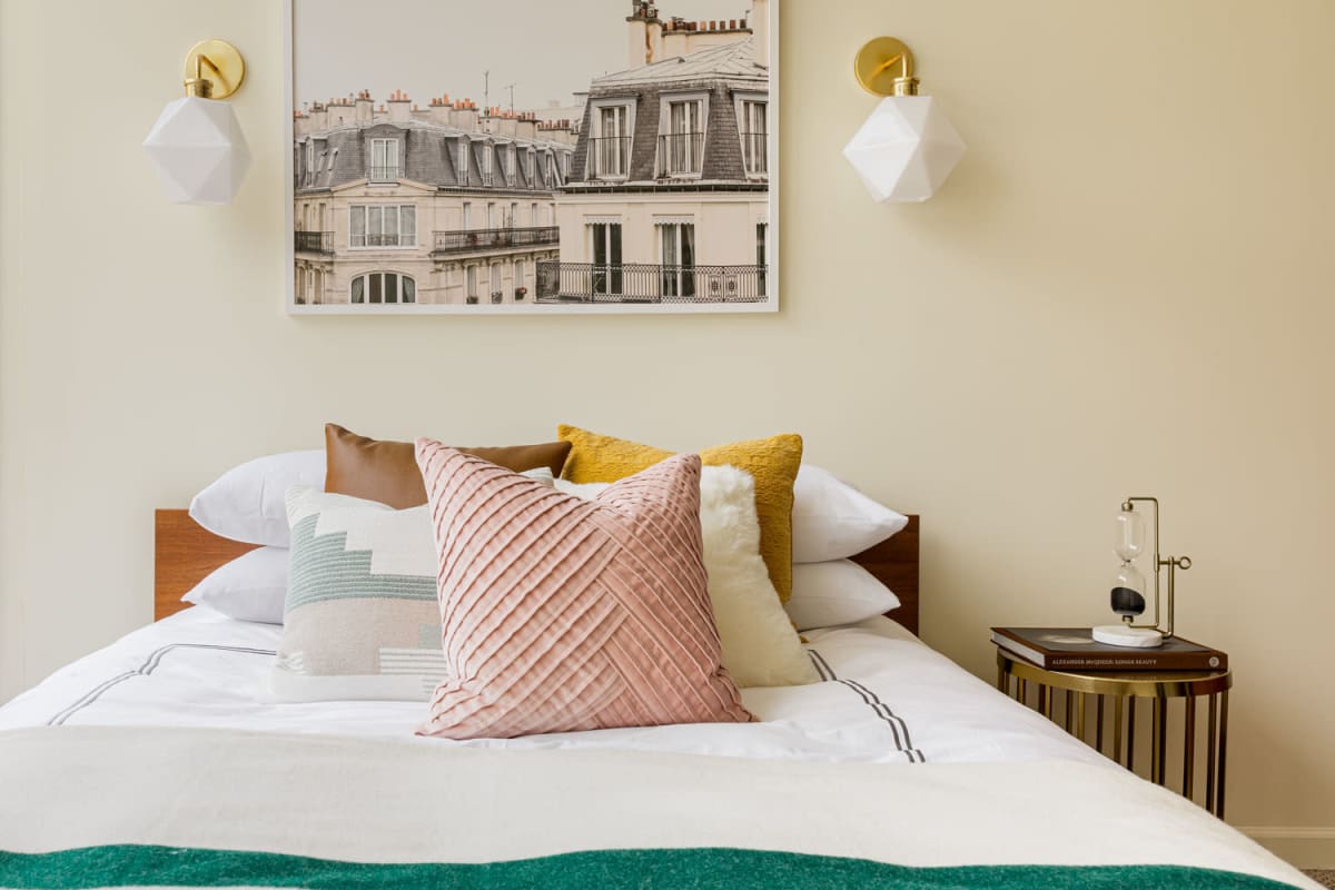 Custom lighting flanking a painting hung above the bed in a model student apartment's bedroom at 20 Hawley in Binghamton, New York