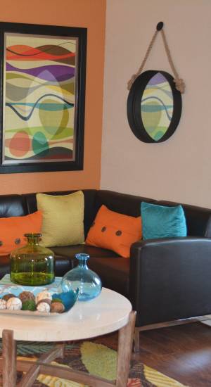 A living room with a comfortable couch with colorful pillows, coffee table with a plant and a round mirror hangs on the wall at The Abbey At Northlake in Riviera Beach, Florida