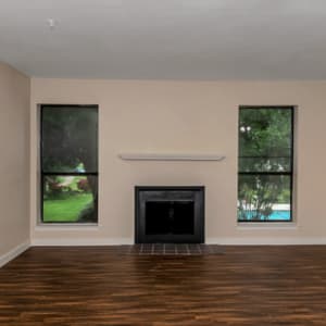 Living room with wood-style flooring and a fireplace overlooking the pool at Stonegate Apartments in Mckinney, Texas