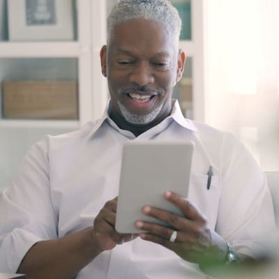 Resident smiling while using a tablet in his home at Mariposa at Bay Colony in Dickinson, Texas