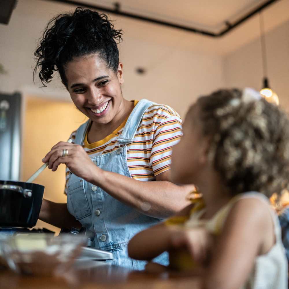 Resident woman cooking with her daughter in the apartment kitchen at Sable Pointe Apartments in Hart, Michigan