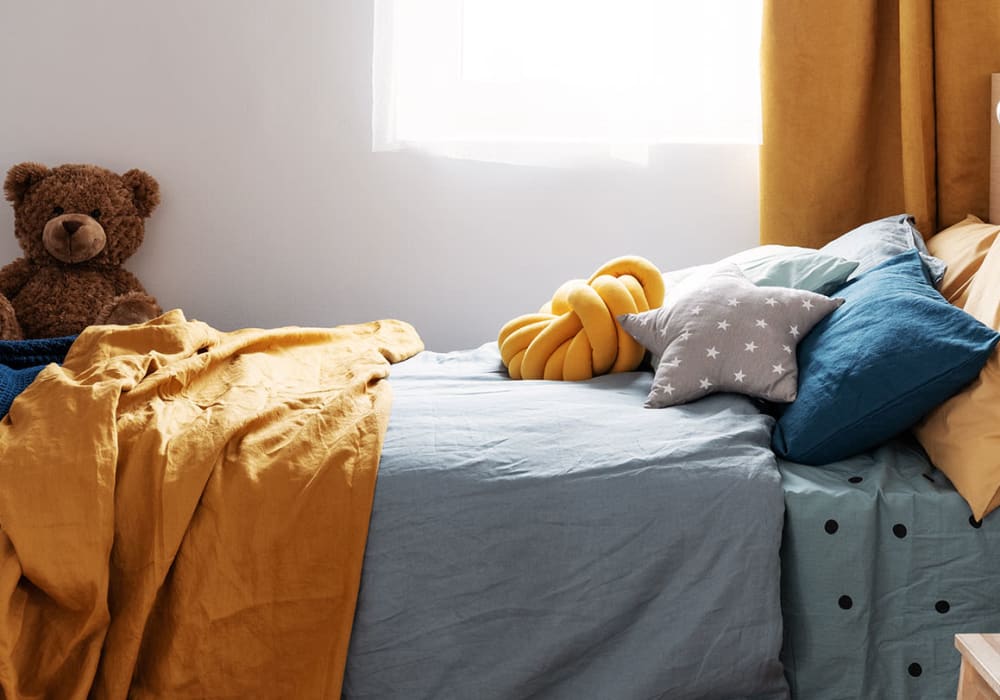 Children's bedroom with twin bed, plush teddy bear, and plenty of sunshine coming through the window at Everwood at The Avenue in Murfreesboro, Tennessee