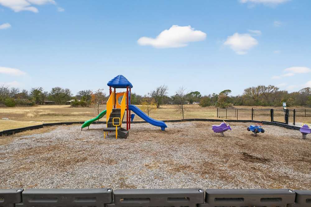 Charming playground featuring vibrant slides and swings, surrounded by spacious greenery at Lakewood Crossing in Granbury, Texas.