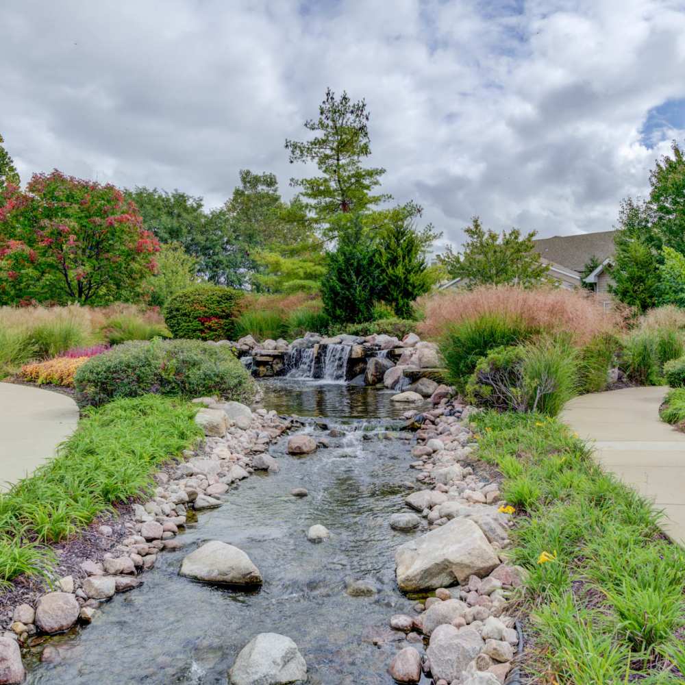 Serene landscaped pathways featuring a charming stone waterfall and lush greenery at Boulder Springs in Maryland Heights, Missouri.
