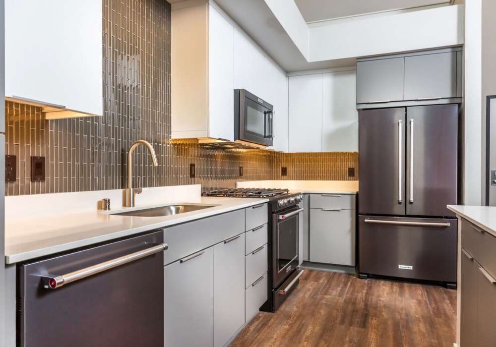 Kitchen with range, refrigerator, dishwasher and wooden cabinets at The George Apartment Homes in Anaheim, California