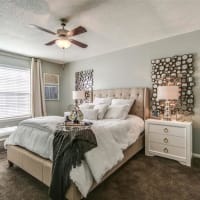Bedroom with large bed and sunshine peering in through the windows at London House Apartments in Lenexa, Kansas