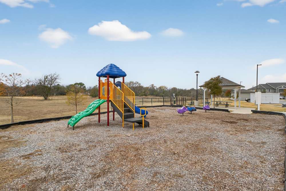 Charming playground with colorful slides and swings, surrounded by open space at Lakewood Crossing in Granbury, Texas.