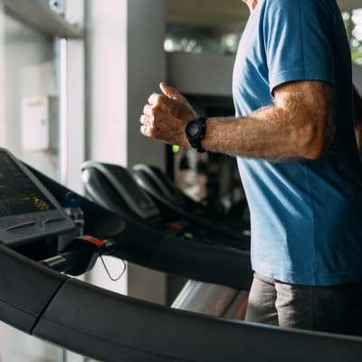 Man jogging on treadmill in a modern fitness center with large windows at Valley Brook Townhomes in Rochester, New York