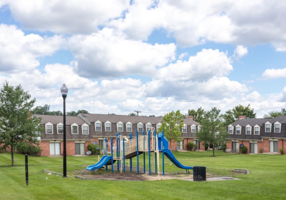 Playground with slides in green lawn area surrounded by apartment buildings and cloudy sky at Dutch Village Apartments in Baltimore, Maryland