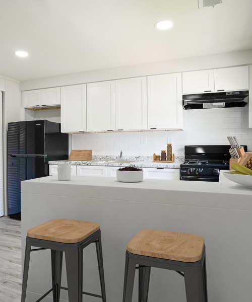 Modern kitchen with granite countertops, stainless steel appliances, and two wood-style bar stools at Dutch Village Apartments in Baltimore, Maryland