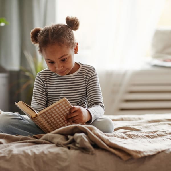 A young girl reads a book in her bedroom at The Amber at Greenbrier, Chesapeake, Virginia