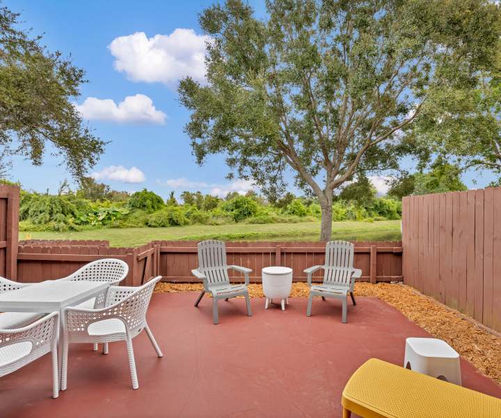 Outdoor patio with seating, surrounded by greenery and a wooden fence, ideal for relaxation at Carlton Arms Of Winter Haven in Winter Haven, Florida