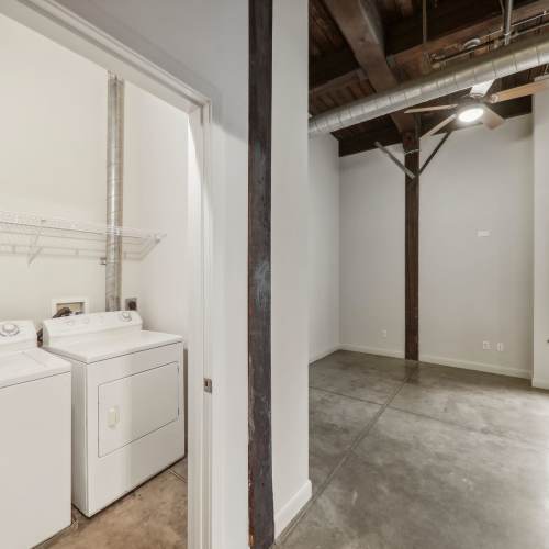Laundry room with stackable washer and dryer and view to unfurnished bedroom at Stadium Loft Apartments in Saint Louis, Missouri