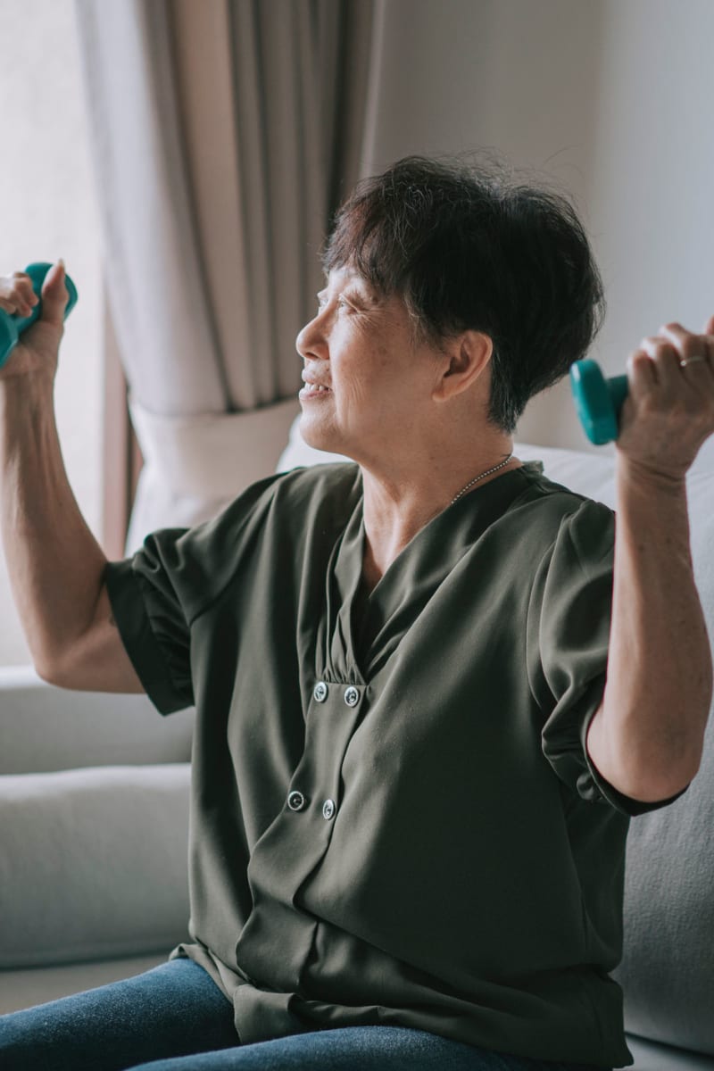 Resident sitting on her couch working with hand-weights at Fair Oaks Health Care Center in Crystal Lake, Illinois